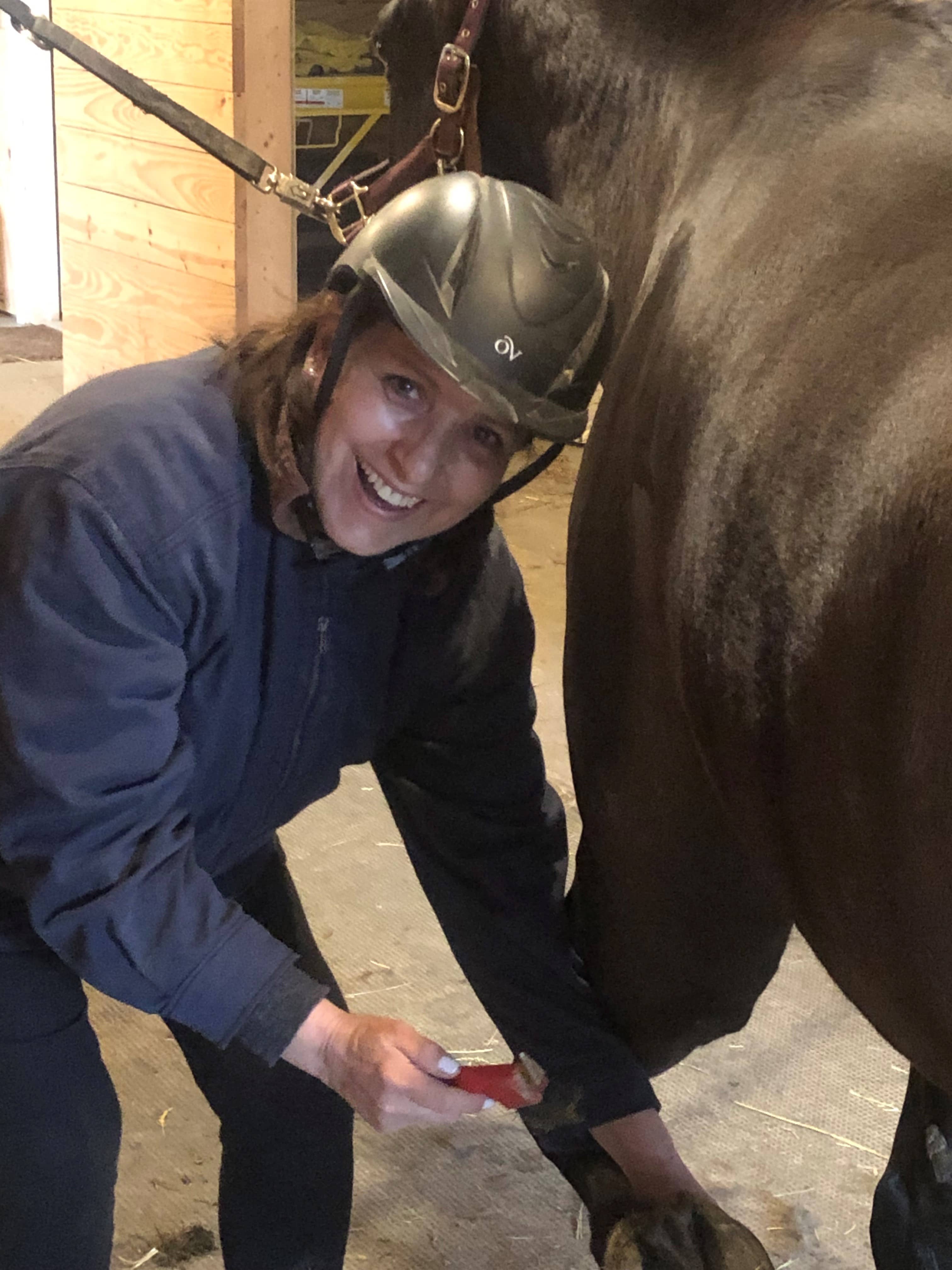 young woman laughing as she cleans her horse's feet
